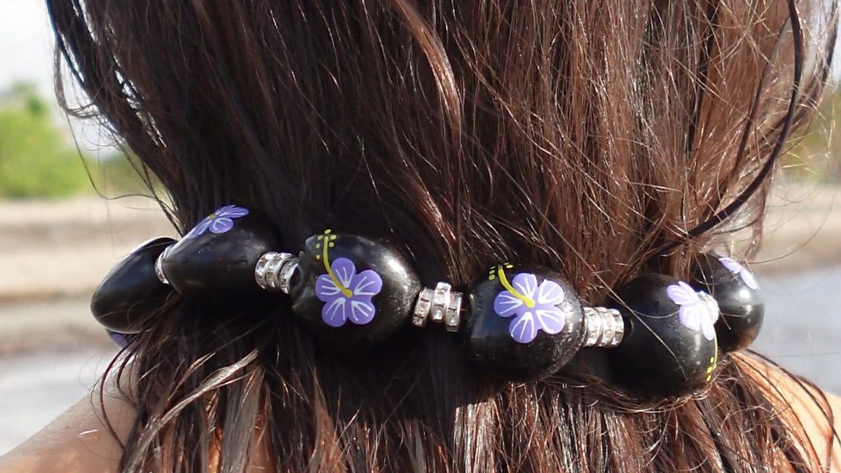 A close-up of a black beaded hair accessory with purple flower details and silver spacer beads, worn around a person's dark brown hair.